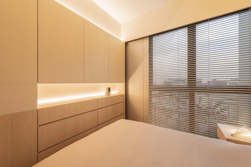 主人房的一面墙是定制的无印良品风极简柜子，搭配精心设计和调校的灯光及同色系的落地百叶窗。