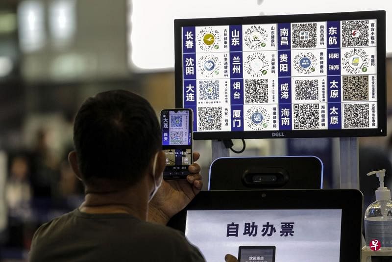 星期一在上海虹桥国际机场，一名搭客在自助办票机前，拿手机扫描其他城市的防疫健康二维码。（彭博社）