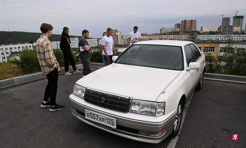 图为汽车供应商和买家9月13日在俄罗斯港口城市符拉迪沃斯托克（Vladivostok）的一条街道上检查一辆二手车。（法新社）