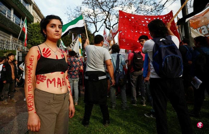 2022年9月，22岁的阿米尼在被拘留期间死亡，随后伊朗国内爆发了示威活动。图为一名示威者脱去上衣和头巾，在伊朗驻阿根廷大使馆前示威。（路透社）