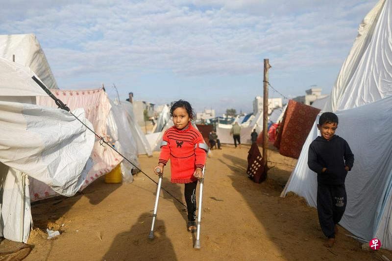 以哈战火持续蔓延，在加沙地带，大量儿童虽侥幸躲过致命炮弹，但却永远失去腿脚。图为一名巴勒斯坦孩童，拄着拐杖走在加沙难民营中。（路透社）