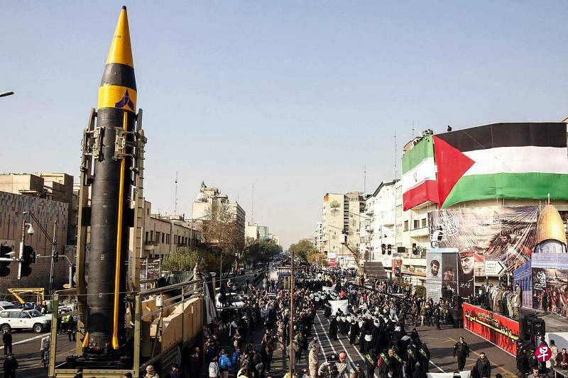 伊朗民众和民兵组织“动员队”（Basij）成员2023年11月24日在德黑兰游行，声援巴勒斯坦人，游行队伍经过一枚“海巴尔”弹道导弹旁。（法新社）