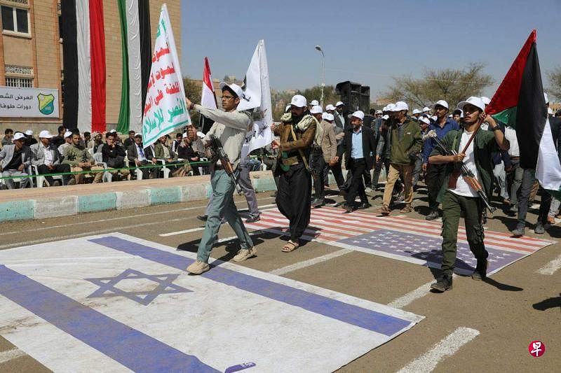 2月21日，也门萨那大学的学生在校园内举行募兵游行，以色列、美国和英国（未出境）国旗铺在地面上，学生们在上面踏步而行。（路透社）