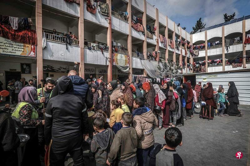 自以哈冲突升级以来，加沙的流离失所者在320多所学校内避难。图为2月19日，流离失所的巴勒斯坦平民在加沙南部拉法市的一所政府学校内，排队领取食物。（法新社）